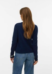 Námořnicky modrý svetr s kulatým výstřihem a dlouhými rukávy, s pružnými manžetami. Kombinován s světle modrými džínami s vysokým pasem.