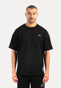 Camiseta negra de manga corta hecha de algodón. Presenta un cuello redondo y un pequeño logo blanco en el lado izquierdo del pecho. Dobladillo recto.