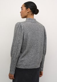 Sivi pulover od vune s visokim ovratnikom, napuhanim rukavima i rebrastim manžetama. Mekana tekstura s estetikom udobnog odijevanja.