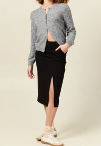 Szary dziergany kardigan, czarna ołówkowa spódnica z bocznym rozcięciem, białe trampki z beżowymi akcentami oraz jasne skarpetki.