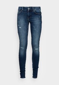 Jeans skinny feitos de denim azul escuro. Apresenta áreas desgastadas e um design clássico de cinco bolsos com fecho de botão.