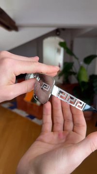 Manos sosteniendo gafas de sol plateadas con varillas de patrón geométrico y lentes rectangulares transparentes en interiores.