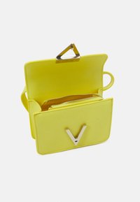 Geel leren handtas met een driehoekige zilveren sluiting, een binnenzak met rits en een voorklep met een zilveren "V" logo.