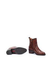 Botas de cuero marrón hasta el tobillo con puntera cuadrada, cremalleras doradas y un tacón texturizado. Presenta un interior con un patrón y una suela de goma con agarre.