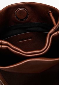 Interno di una borsa in pelle marrone con texture morbida, caratterizzata da una foderatura nera e una chiusura circolare. Logo "Massimo Dutti" impresso visibile.
