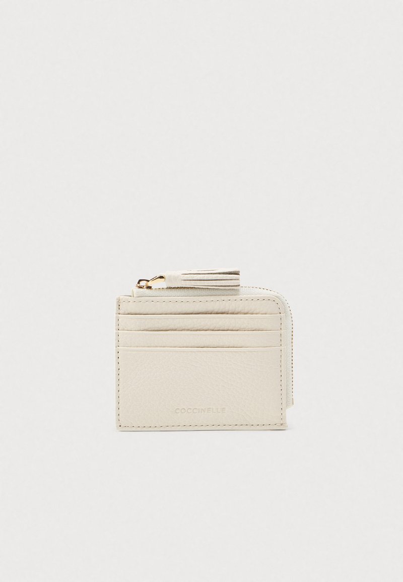 Tiivis kermavalkoinen nahkakorttikotelo, jossa on neljä korttipaikkaa, vetoketjullinen osio ja tupsuvetoketju.