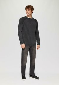 Dunkelgrauer Pullover mit Raglanärmeln, gerippten Bündchen und Bund. Kombiniert mit hellgrauen Jeans und schwarzen Turnschuhen mit weißen Sohlen.