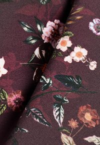 Bloemmotief stof met een donkere bordeauxrode achtergrond en roze, witte en groene bloemen, gestructureerde weving en opvallende bladranden.