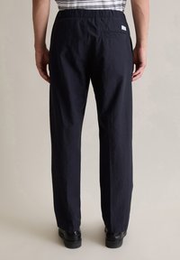 Marineblauwe, lichtgewicht broeken met een relaxte pasvorm, elastische tailleband en een achterzak. Zachte textuur, lichte glans en stevige constructie.