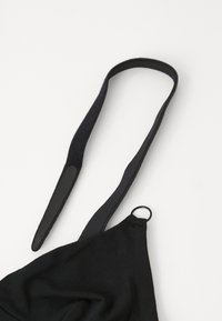 Μαύρος υφασμάτινος ιμάντας με ματ φινίρισμα, που διαθέτει μια υφή και μια μεταλλική λεπτομέρεια, προσαρτημένος σε ένα μαύρο υλικό στοιχείο.