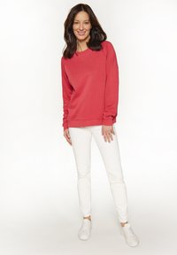 Rode sweatshirt met ronde hals en lange mouwen, gecombineerd met witte skinny jeans en witte sneakers. Glad materiaal en een ontspannen pasvorm.