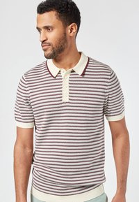 Vaaleanruskea raitapaitainen polo paita lyhyillä hihoilla, jossa on viininpunaisia ja tummansinisiä vaakaraitoja. Ominaisuuksiin kuuluu ribbauskaulus ja kolmonen napitus.