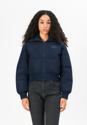Veste puffer courte de couleur marine avec des poignets et un ourlet côtelés, dotée d'un col haut et d'une fermeture éclair à l'avant. Patch de marque discret sur la poitrine.