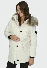 Cappotto imbottito bianco con cappuccio foderato in pelliccia, chiusura a bottoni, vita elastica e dettagli neri. Presenta tasche laterali e polsini a contrasto.