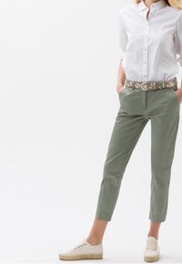 Lättvit skjorta, olivgröna cropped byxor, mönstrat bälte och beige sneakers med vävd sula.