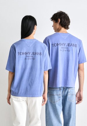 Svetlomodré bavlnené tričká majú okrúhly výstrih a spadnuté ramená, na chrbte sú potlačené tmavosivým písmom "TOMMY JEANS" a rok.