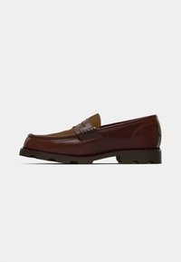 Mocassim de couro castanho e camurça com sola preta grossa e detalhes de costura, apresentado de lado em fundo branco.