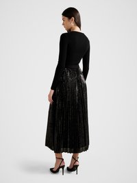 Black ribbed long-sleeve top paired with a pleated black sequined skirt; model wears black ankle-strap heels, showcasing a sleek silhouette.