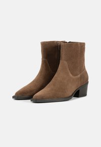 Botas de ante marrón hasta el tobillo con punta afilada, cremallera lateral y un tacón bajo en bloque. La textura es suave con acentos de costura visibles.