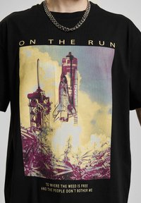 Sort bomulds t-shirt med et farverigt grafisk design af en raket og en affyringsrampe. Inkluderer tekst øverst og nederst. Crew neckline og korte ærmer.