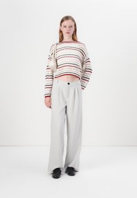 Knit cropped sweater with horizontal red, black, and cream stripes; paired with high-waisted gray wide-leg trousers and black loafers.