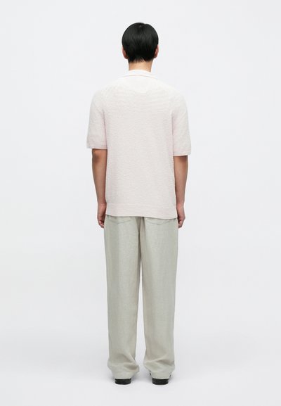 Ανοιχτό ροζ κοντομάνικο πλεκτό πουκάμισο με υφασμάτινη υφή, συνδυασμένο με ανοιχτόχρωμο γκρι, φαρδύ παντελόνι. Απλός, μίνιμαλ σχεδιασμός.