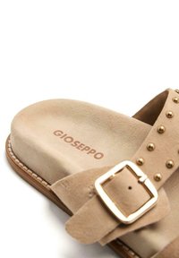 Sandalo in suede beige con una fascia larga decorata con borchie dorate e una fibbia rettangolare dorata. Nome del marchio "Gioseppo" stampato in marrone.