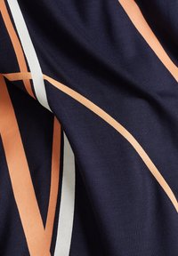 Marinblått tyg med diagonala ränder i persika och vitt. Slät textur med en lätt glans, som visar ett modernt mönster.