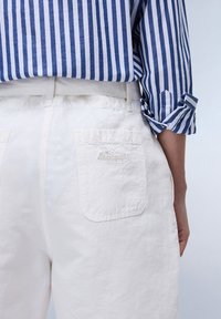 Celana putih dengan permukaan bertekstur dan saku belakang yang menampilkan logo bordir. Dipadukan dengan kemeja lengan panjang bergaris biru dan putih.
