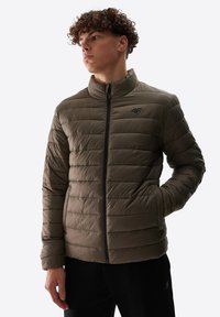 Chaqueta de plumas en verde oliva, diseño acolchado con rayas horizontales, cuello alto, cremallera negra y logo en el pecho.