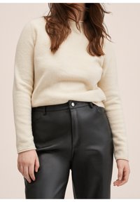 Suéter de color crema hecho de material suave, combinado con pantalones de cuero negros ajustados que tienen una textura lisa y mínimos acentos de hardware.