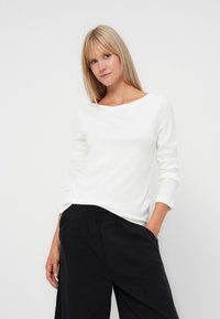 Top de manga larga blanco con un escote barco, combinado con pantalones de pierna ancha negros. Textura suave y ajuste relajado, adecuado para un atuendo casual.