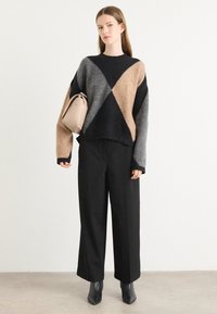 Sweater oversized em malha com blocos de cor em preto, cinza e bege; combinado com calças largas pretas e botas de salto pretas. Bolsa bege.