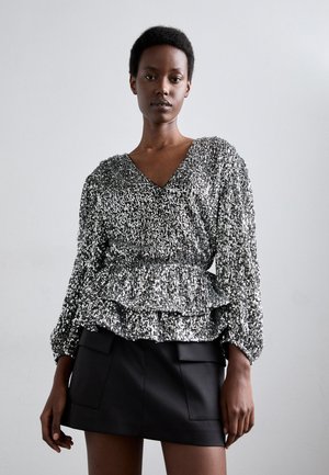 Zilveren paillettenblouse met een V-hals, lange mouwen en een gerimpelde peplum taille, gecombineerd met een zwarte minirok met opgestikte zakken.