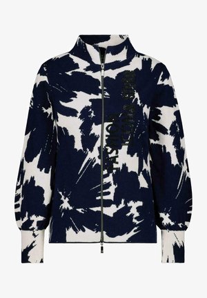 Chaqueta con cremallera de patrón abstracto en blanco y negro, con cuello alto y puños acanalados, con texto vertical en el lado derecho delantero.