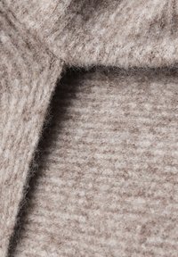 Tissu en laine beige présentant un design texturé avec des fibres visibles et une surface lisse, montrant un motif rayé subtil.