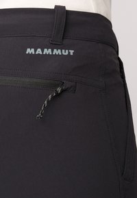 Pantalons noirs avec une poche zippée, d'une texture lisse et un logo MAMMUT en bleu clair sur la taille.