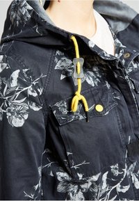 Námořnický sako s květinovým vzorem a šedou kapucí, s žlutou šňůrkou, žlutými knoflíkovými akcenty a dvěma předními kapsami.