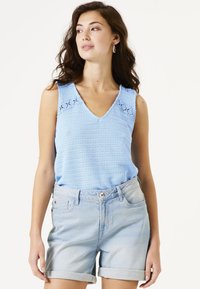 Hellblaues gestricktes Tanktop mit V-Ausschnitt und dekorativer Stickerei, kombiniert mit hochgekrempelten Jeansshorts. Weiche Textur, lässiges Design.