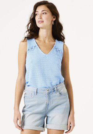 Top in maglina azzurro chiaro con scollatura a V e cuciture decorative, abbinato a pantaloni di jeans corti arrotolati. Texture morbida, design informale.
