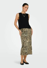 Zwarte geribbelde crop top gecombineerd met een satijnen midi-rok in luipaardprint, met een getailleerde silhouet en zwarte platte schoenen.