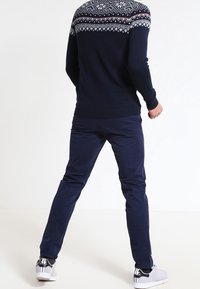 Marineblauw trui met witte geometrische patronen op de schouders, gecombineerd met marineblauwe broek en grijze sneakers. Eenvoudig, functioneel ontwerp.