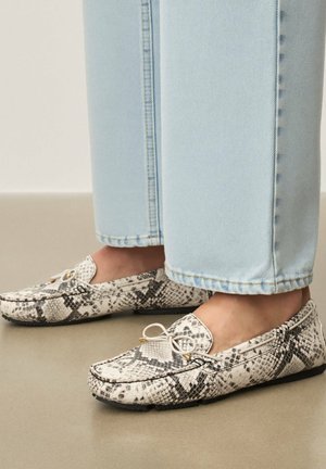 Texturált mokaszin kígyómintás mintával, bézs alapon fekete részletekkel, lekerekített orral és díszes masnival a tetején.