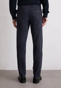 Dunkelblaue Hose aus weichem Stoff, mit geradem Schnitt, aufgesetzten Taschen mit Knöpfen und einer glatten Textur.
