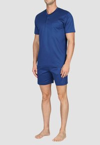Camicia blu navy a maniche corte con scollo rotondo e una tasca sul petto, abbinata a pantaloni corti coordinati, realizzata in un tessuto leggero e liscio.