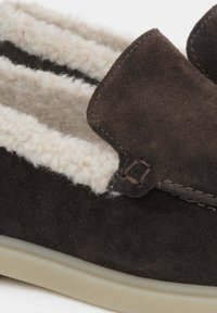 Brązowy zamszowy kapcie z kremowym futerkiem, z przeszywaną krawędzią i małym skórzanym akcentem. Gładka, lekka podeszwa.