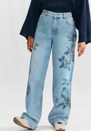 Helleblaue Denim-Jeans im weiten Schnitt mit floralem Druck auf der linken Seite und einem verwaschenen Look. Mit einem Metallknopf und einem Reißverschluss verschlossen.
