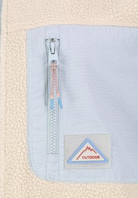 Fleece bunda s krémovou texturou, světle modrou látkovou částí, předním zipem se růžovými a modrými táhly a trojúhelníkovou nášivkou "OUTDOOR".