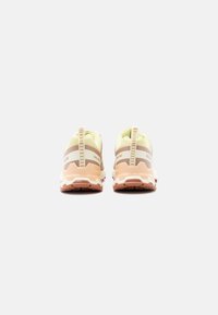 Par tekaških copat v bež, beli in roza barvi, prikazanih od zadaj, z teksturiranimi podplati in zanke za poteg na belem ozadju.