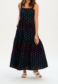 Black dress with a tiered design, featuring multicolored polka dots in pink, blue, green, and orange. It has adjustable shoulder straps and pockets.